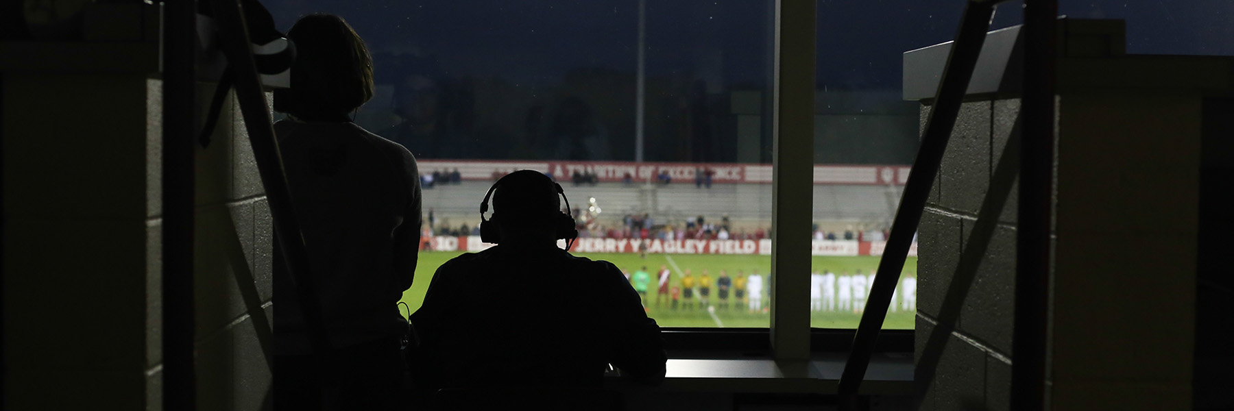 Announcers comment on a soccer game, back to camera.