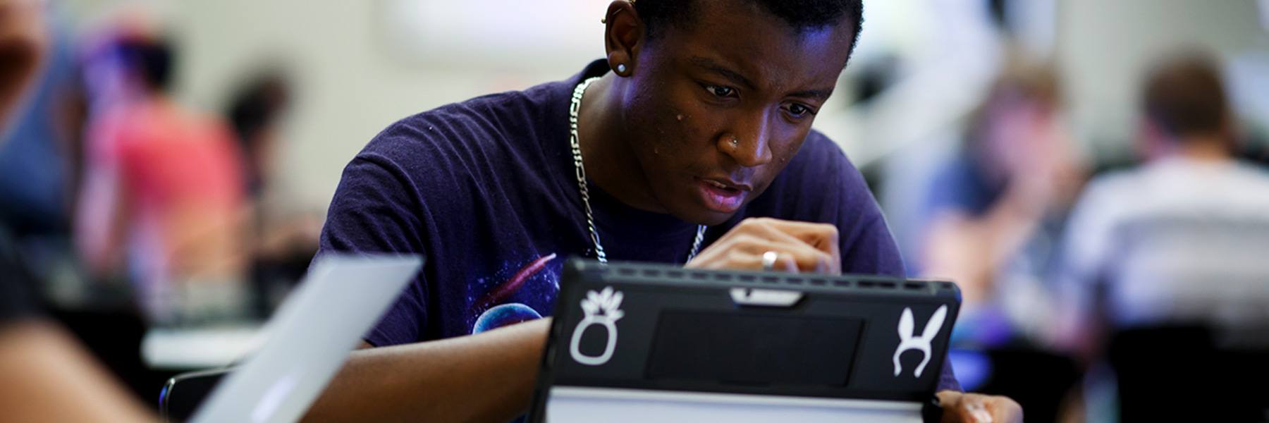 A student works on a graphic drawing tablet in a class with other students working behind him.