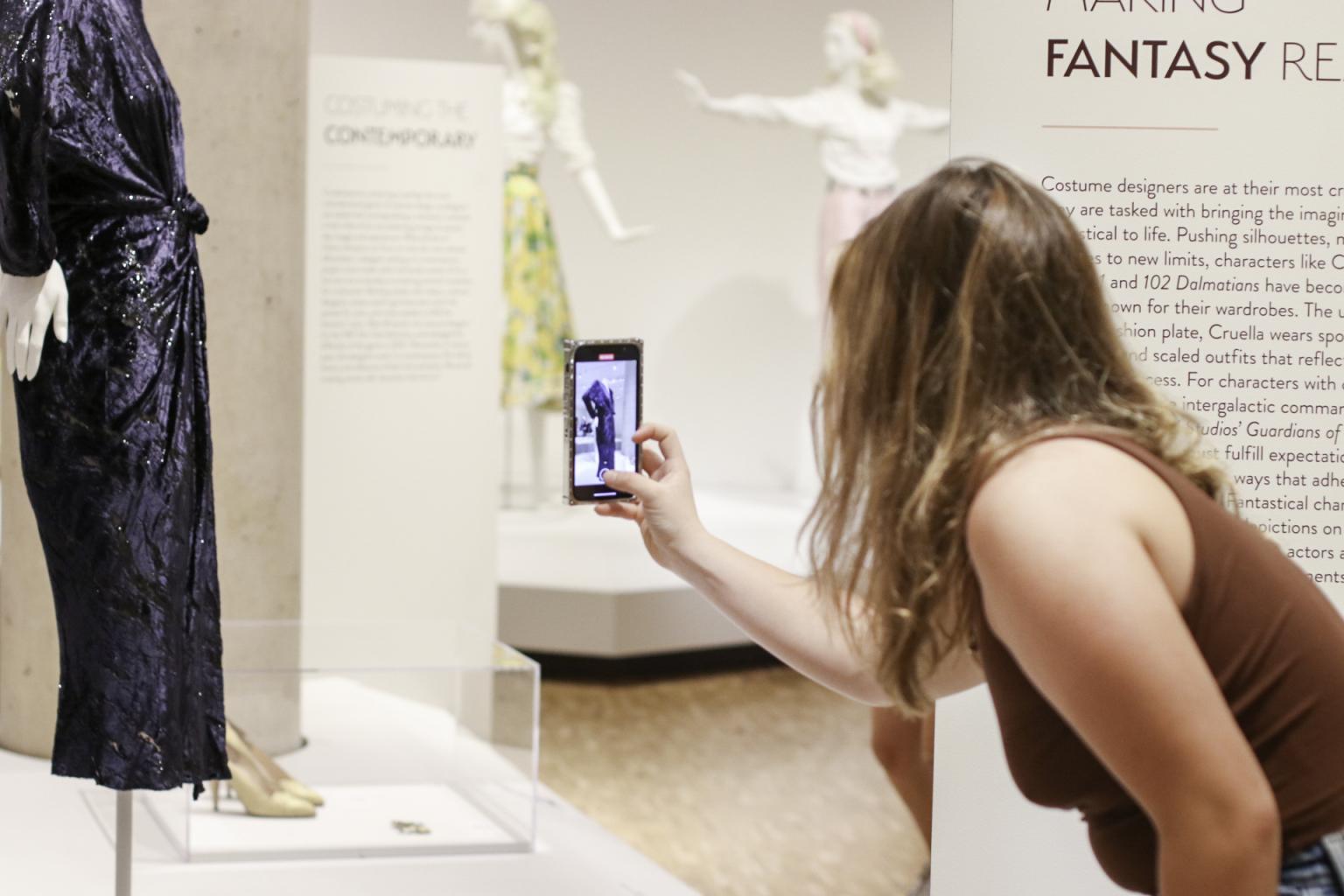 A student takes a photo of a costume design in Eskenazi.