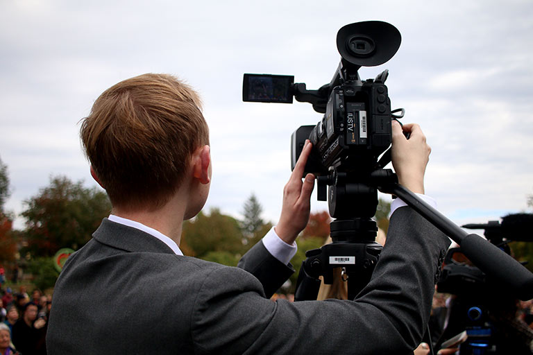 A student in a suit uses a video camera outside.