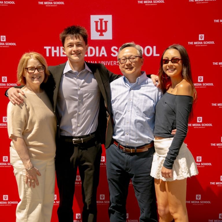 Four people stand in front of a backdrop with the IU logo repeated several times.