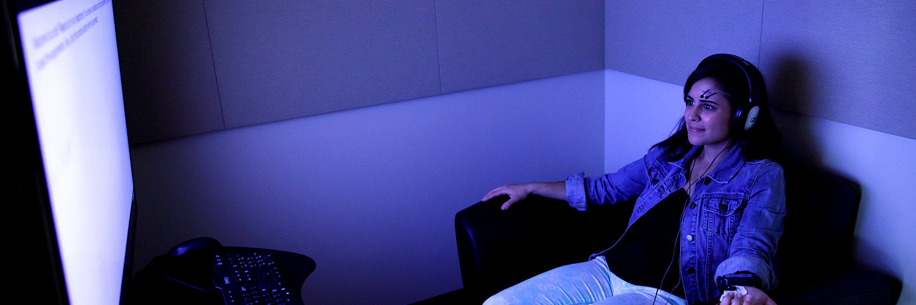 A person wearing a headset and electrodes sits in front of a screen.