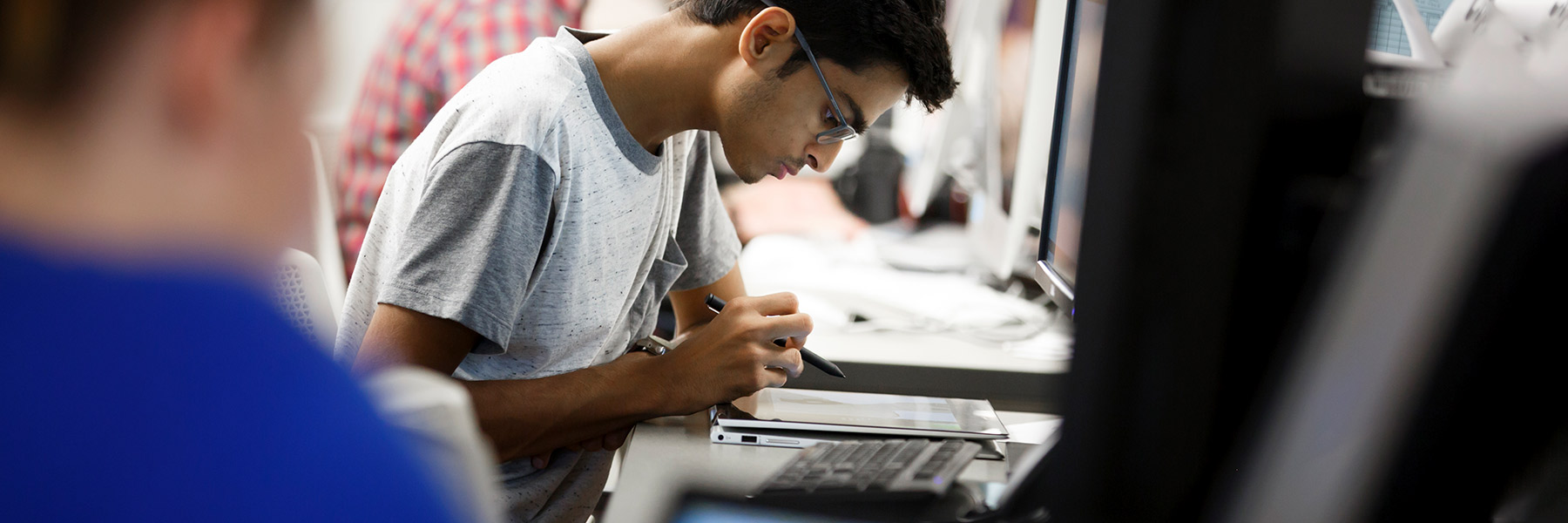 A student sits and uses a stylus on the tablet in front of him