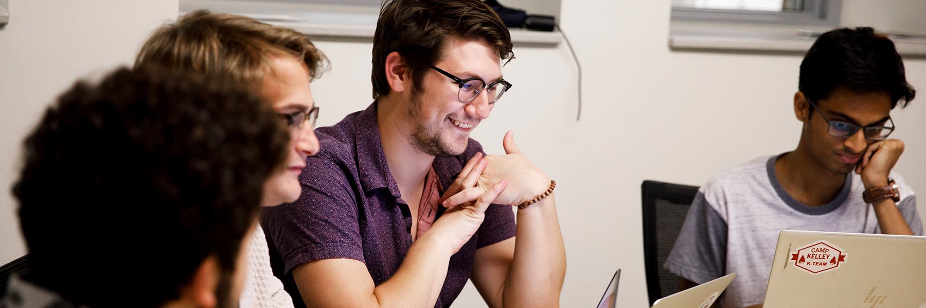 A group of students sit around a table with laptops open in front of them.